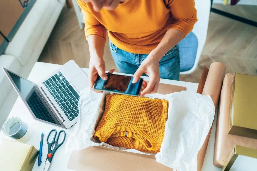 Person photographing yellow jumper for online selling.