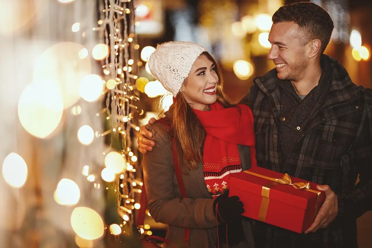 Happy couple with Christmas gift and lights at night.