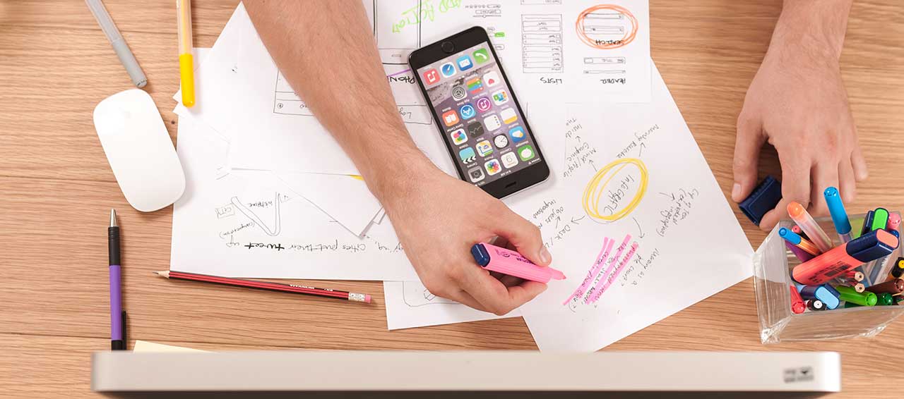 Person organising notes with smartphone on desk.