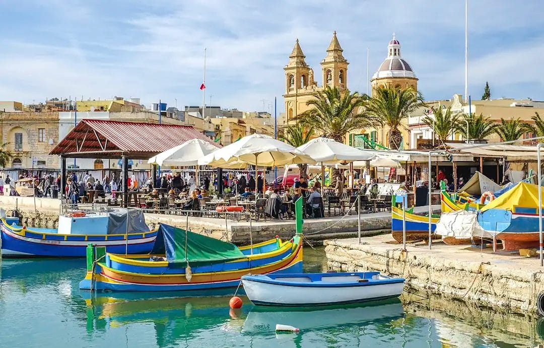 Colourful boats in Maltese waterfront village scene.