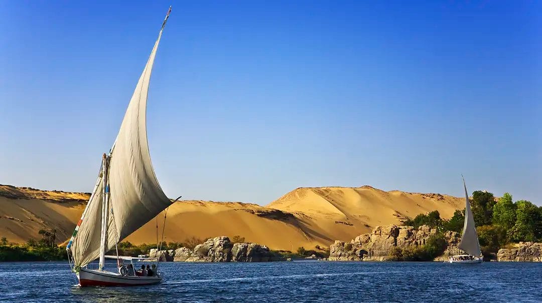 Sailboats on the Nile River near desert dunes.