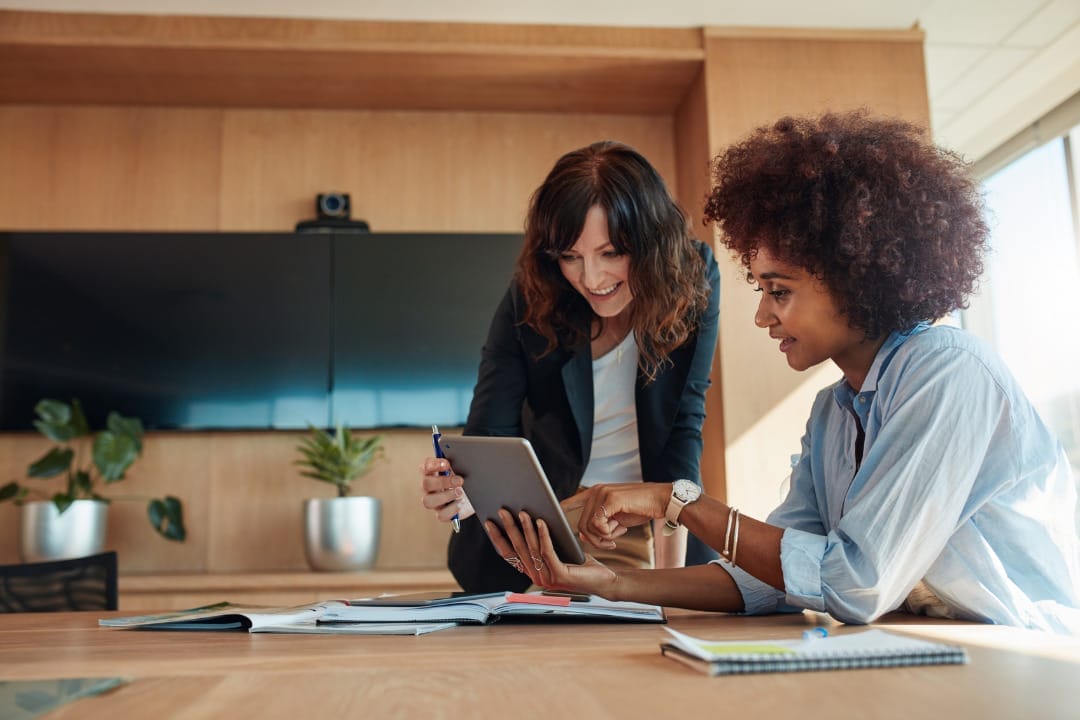 Two women collaborating on tablet in office.