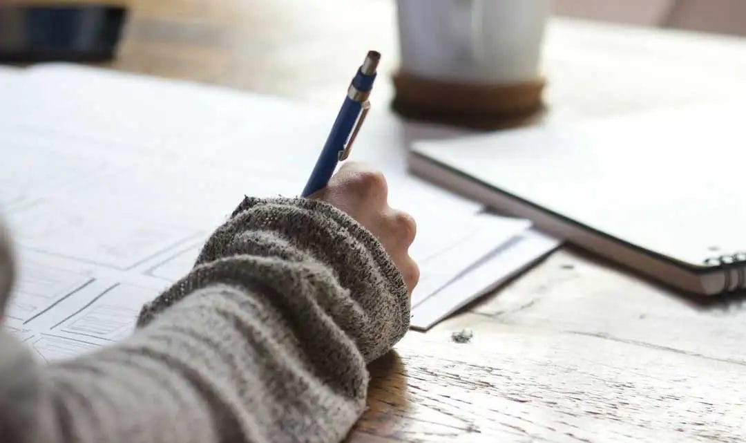 Person writing notes at a wooden desk.