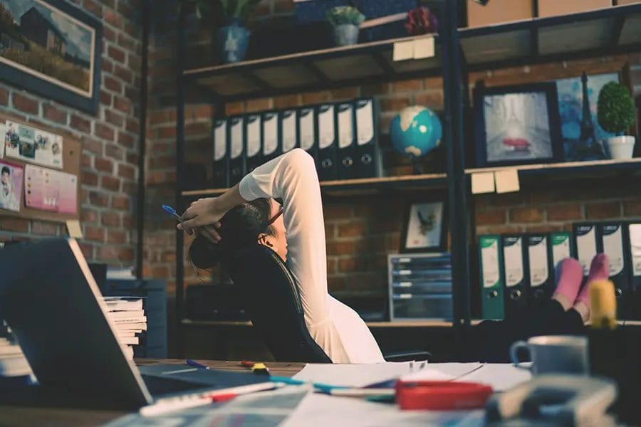 Worker stretching in office chair, hands behind head.