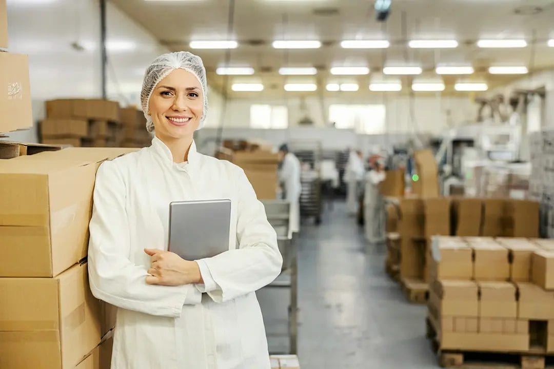 Woman in lab coat holding tablet in warehouse