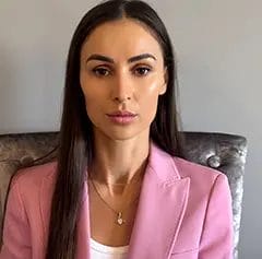 Woman in pink blazer, neutral expression.